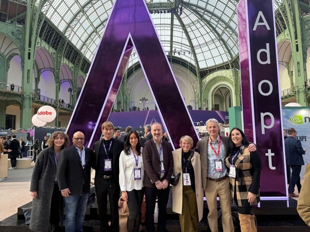 Group photo of Canada’s delegation at the Adopt AI Summit in Paris, standing in front of a large purple “A” installation inside the Grand Palais. Brian Simmers is standing third from the right among the delegation members.