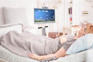 Patient in a hospital bed using a MindfulGarden device displaying calming nature visuals to reduce delirium and agitation